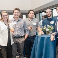 GVSU Alumni stand smile at camera and stand around table. One man is leaning on table.